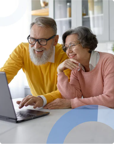 Casal feliz de idosos sorrindo enquanto usa um laptop na cozinha, mostrando a interação entre gerações e a tecnologia moderna.