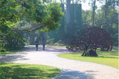 Caminho tranquilo em um parque com escultura de árvore e pessoas caminhando, ideal para relaxar e apreciar a natureza.