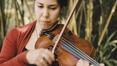Mulher tocando violino em um ambiente natural, concentrada e demonstrando habilidade musical enquanto aproveita a música em meio à natureza.