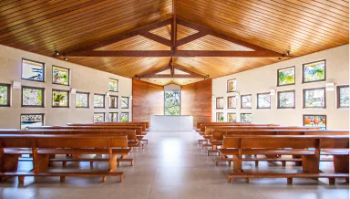 Igreja moderna com interior amplo e luminoso, featuring janelas que proporcionam luz natural, bancos de madeira e um altar minimalista.